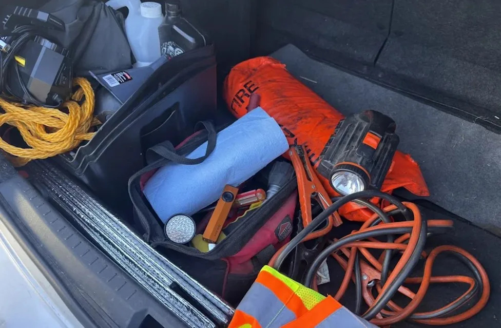 Driver checks car emergency kit, finds flashlights missing, knotted rope, and outdated jumper cables